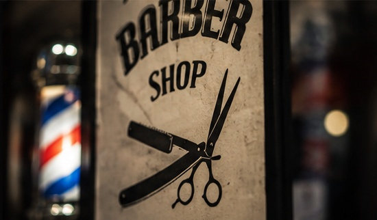 A weathered Barber Shop sign with a straight razor and scissors, lit barber pole beside it