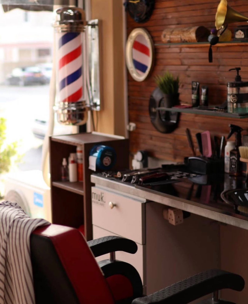 The red white and blue barber pole in the front window beside a work station of combs, clippers and muk products